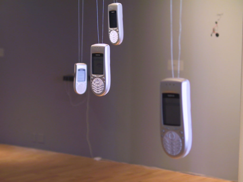 photograph of an installation called 'Media Minatures' in New York. photo shows mobile phones hung from the ceiling, where audiences could engage with the collections.